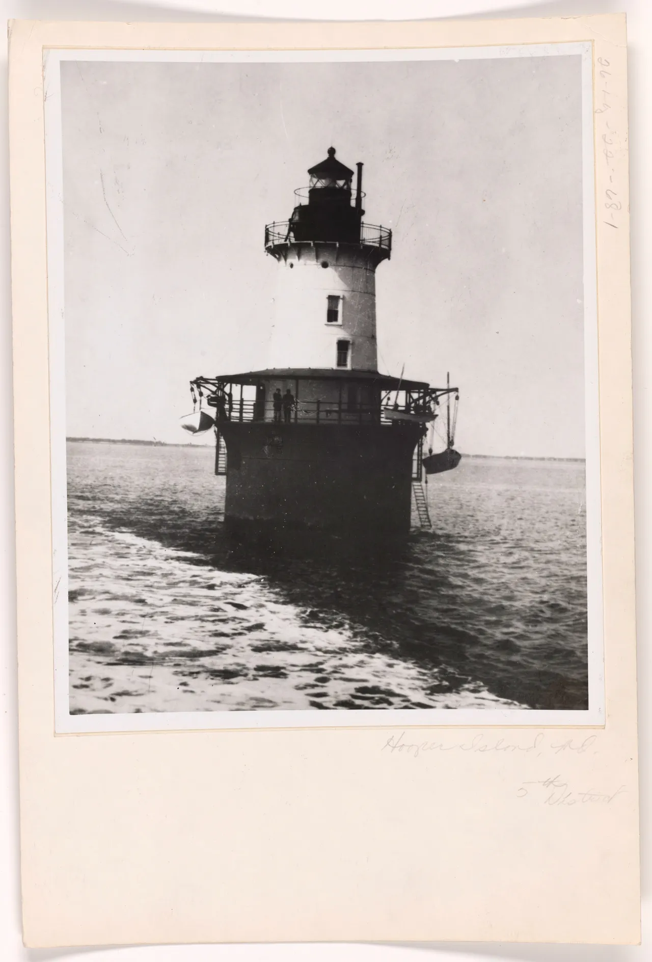 An old black and white photograph of Hooper Island Lighthouse showing the tower, a wide deck around the base and a small boat alongside.