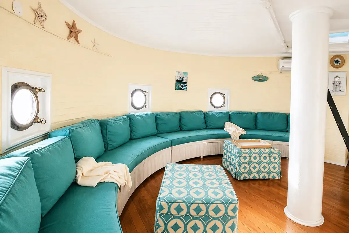 The round port room converted to a living area, with a curved teal sofa following the wall, brass portholes and a white central column.