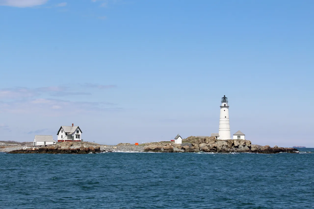 Little Brewster Island from a passing ferry with the white tower, the keeper's house and outbuildings low on the horizon.