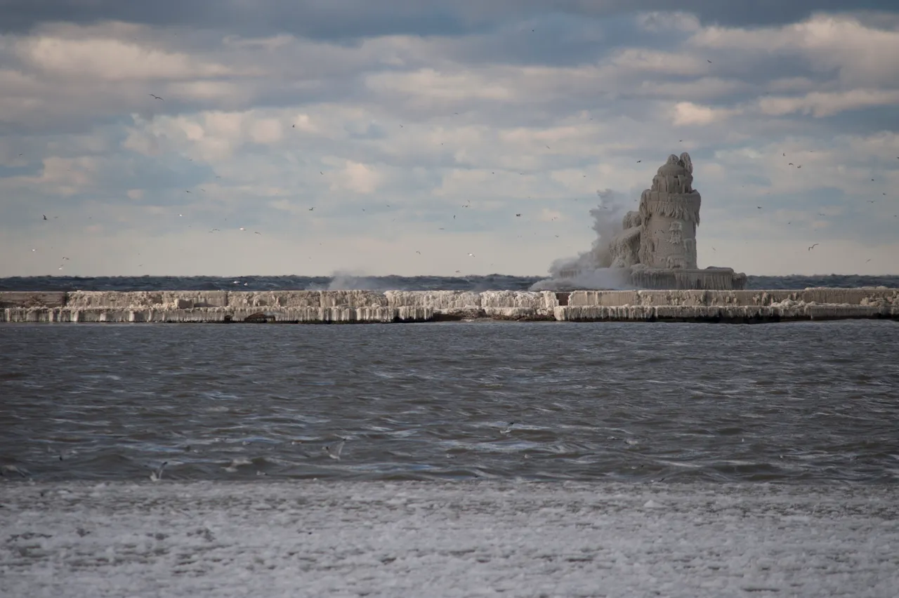 A huge wave bursting against the lighthouse on the Cleveland breakwater during a winter storm with cold spray blowing across.