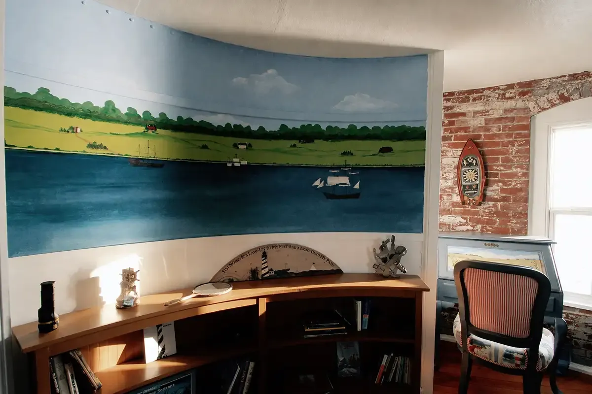 The sleeping quarters with a painted mural of a river landscape across the curved wall, a built-in desk and an exposed brick wall.