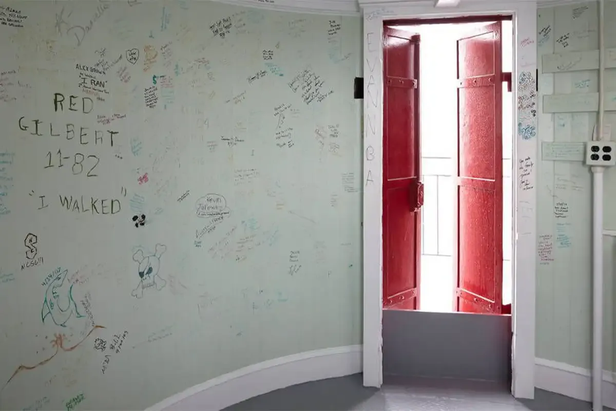 The watch room with pale green walls covered in decades of handwritten signatures and a pair of red doors open to the gallery.