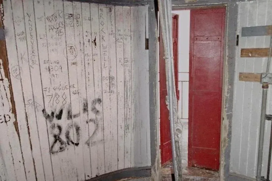 The watch room before restoration with scratched and graffiti-covered white walls and a red door.