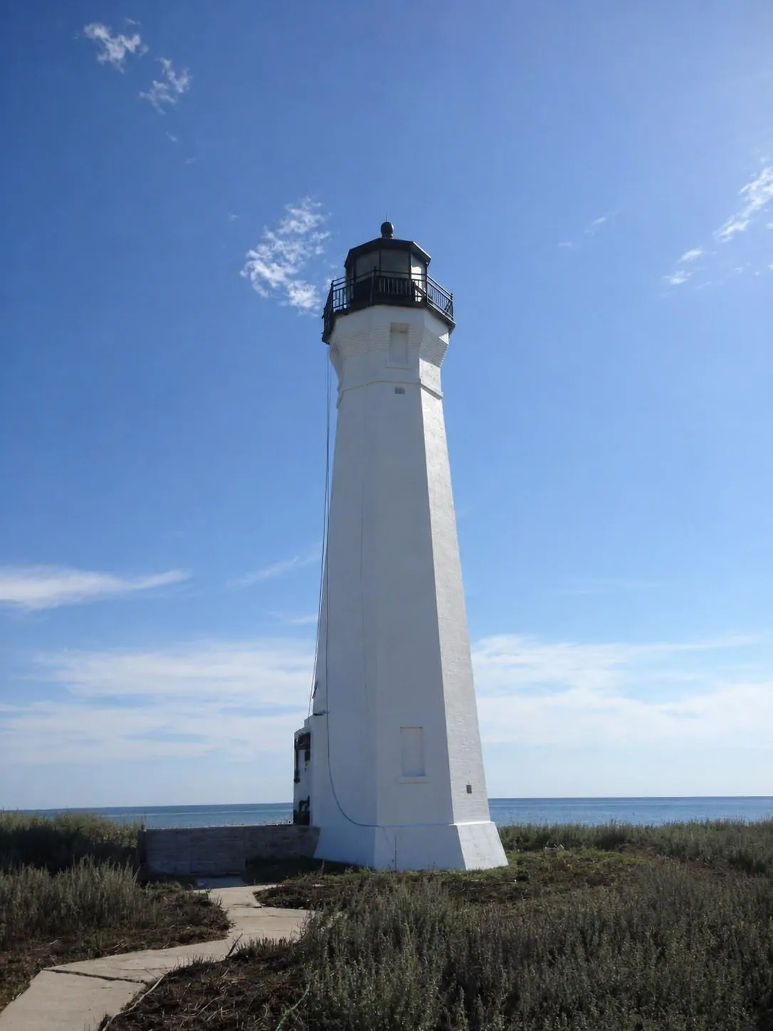 Skillagalee Lighthouse, a white octagonal tower with a black lantern, seen from a path across the gravel island under a blue sky.