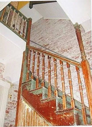 Original wooden staircase with a railing turning up through a wall of exposed painted brick.