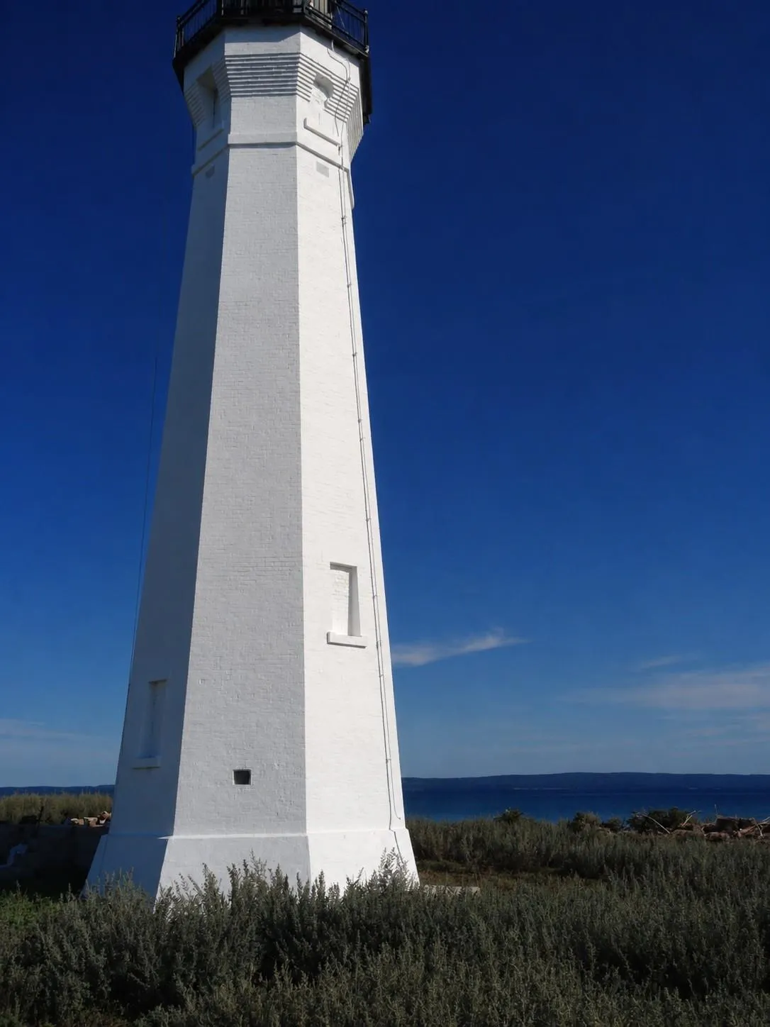 Skillagalee's white octagonal tower seen from the base looking up, with a lantern room at the top and dune grass in the foreground.