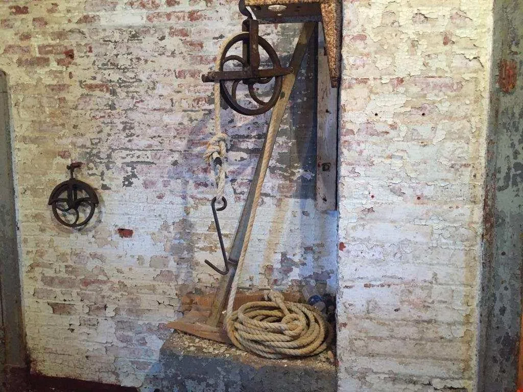 A brick basement wall with a hand winch, rope and pulleys.