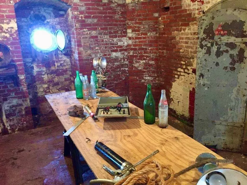 A workbench in the brick-walled basement with tools and bottles, lit by a bright lamp.