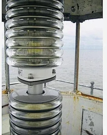 The stacked glass rings of a lantern-room lens beside the gallery railing.